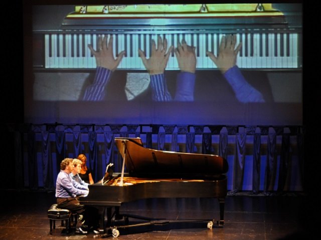 Two piano players at a grand piano on stage.