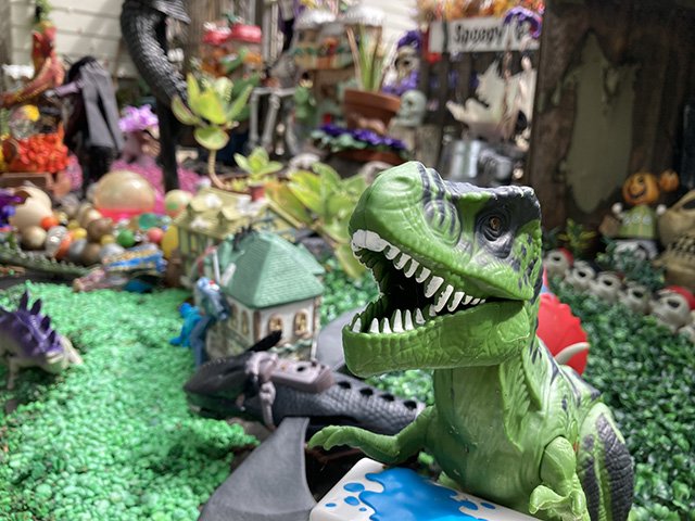 A T. Rex dinosaur toy roars in front of a castle and more in the Spoopy Garden.